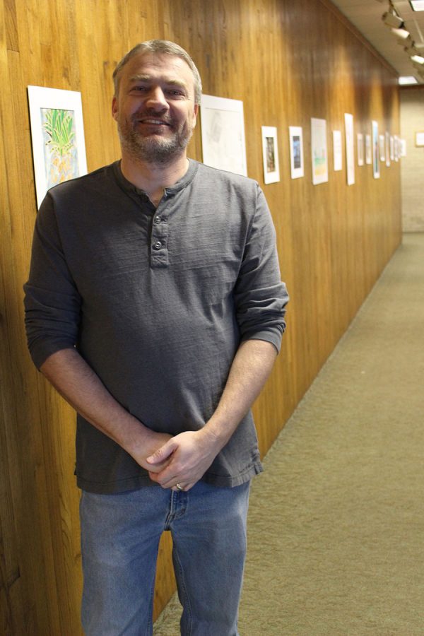 Art instructor Dustin Farmer smiles big in front of art projects.