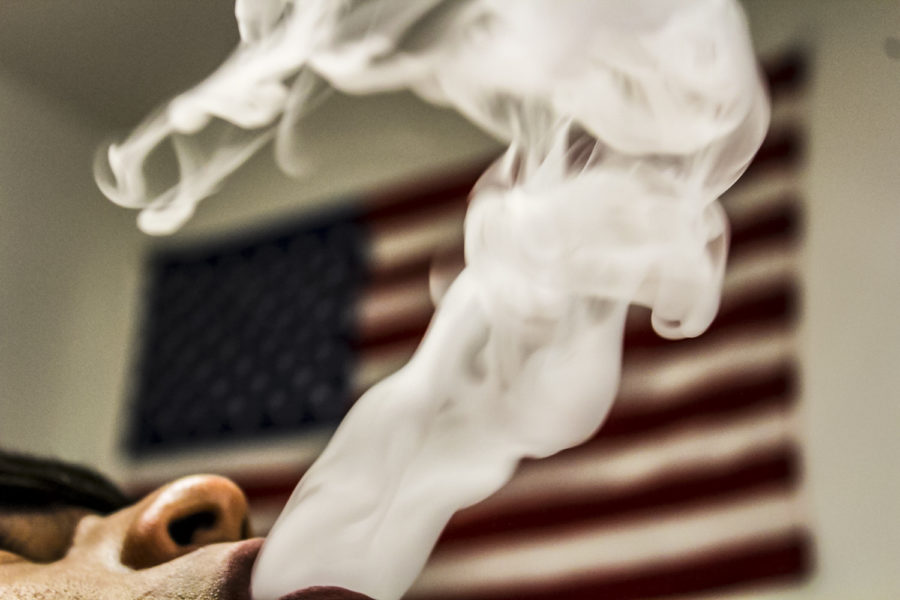 As+a+vapor+cloud+rises+in+the+air%2C+an+American+flag+hangs+proudly+behind+it.+With+47+states+already+having+restrictions+such+as+no+indoor+vaping%2C+people+are+showing+initiative+to+make+a+change+in+the+nation.+Massachusetts+has+even+took+steps+further+and+banned+the+sale+of+all+vaping+products+for+four+months.