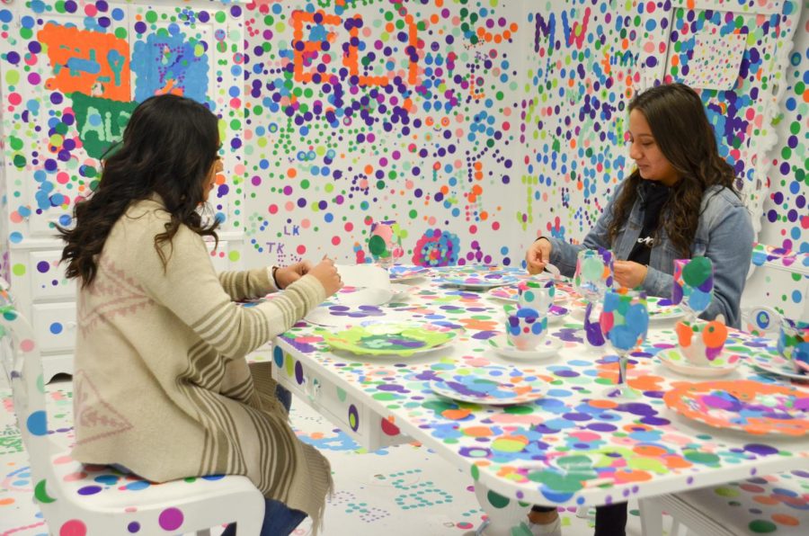 Karina Rodriguez and Denisse Delgado, both freshmen from Hugoton, add their own stickers to the colorful room at Baker Arts Center. This room features just normal round stickers that patrons add to the white surfaces to create an art exhibit.
