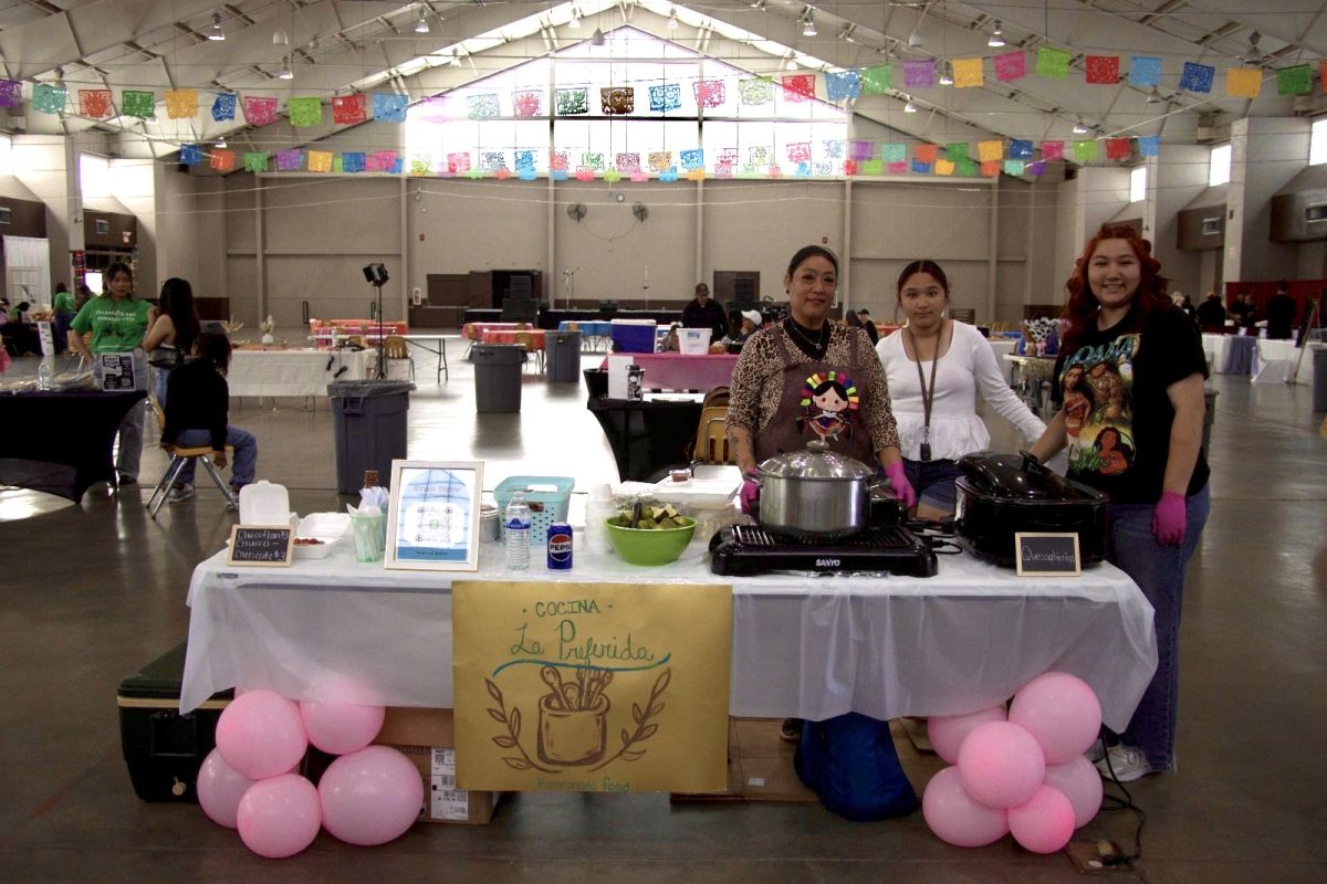 Representatives from “Cocina La Preferida” smile behind their booth offering homemade food at the Celebrate and Connect Fest. The setup included hot dishes and festive balloon decorations.
