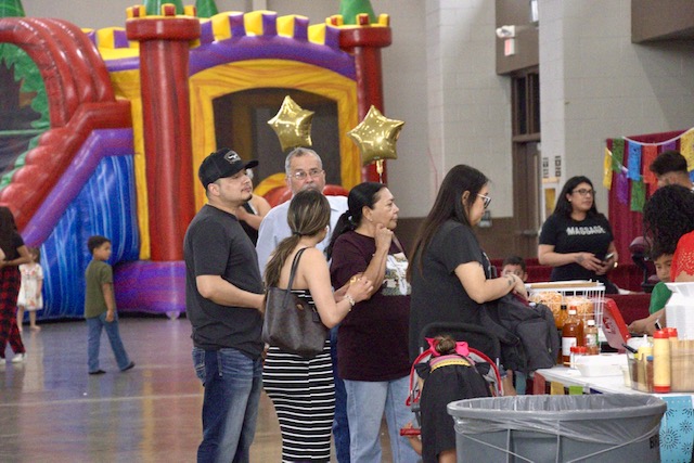 Families line up at a Elotes Fuereno booth during the Celebrate and Connect Fest, with a bounce house in the background adding to the fun, family-friendly atmosphere.