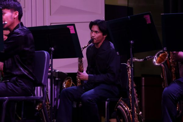 A student musician sits on stage holding his saxophone as he performs "Let the Lights of Christmas Shine" during the concert. He watches his director, Thompson, closely to stay in time with the music.